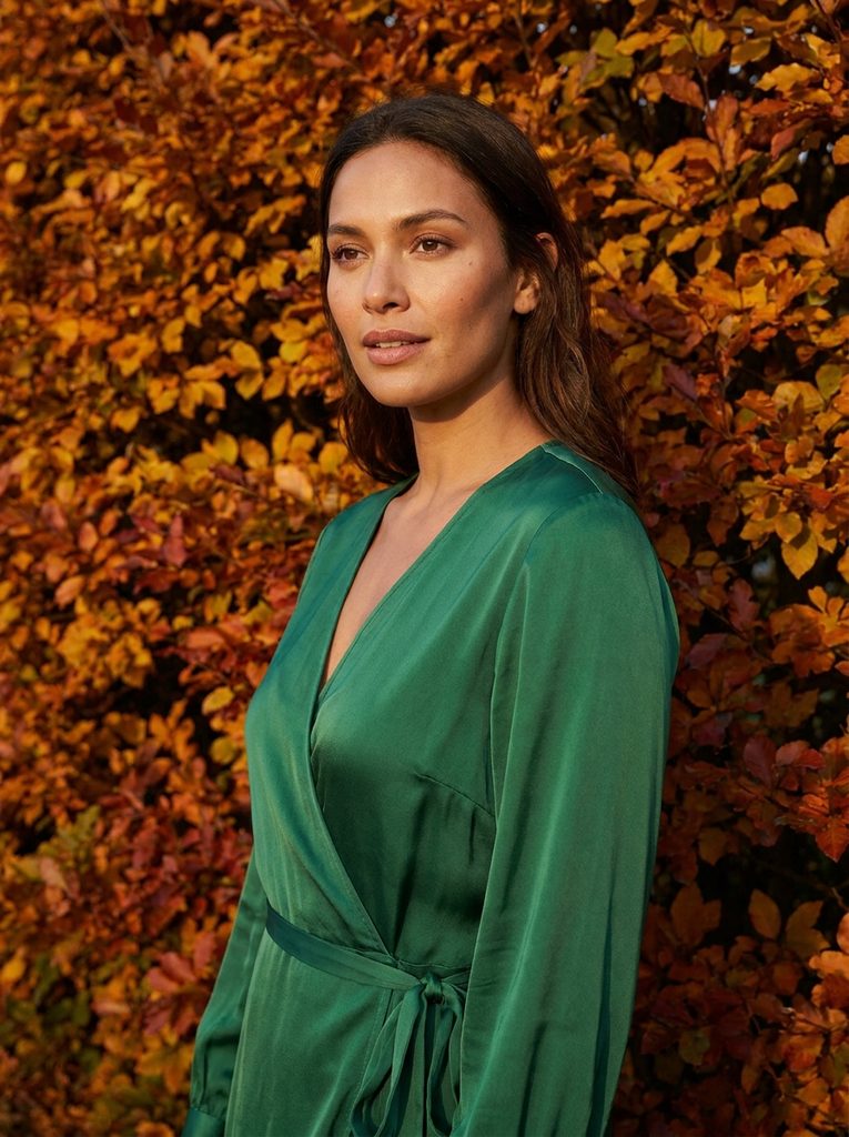 Woman wearing an emerald green dress for a fall wedding among autumn leaves