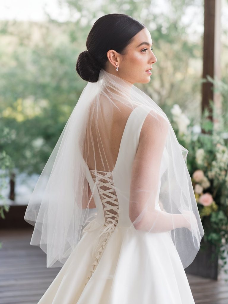 Bride with a smooth low bun wearing a tulle veil outdoors in natural light