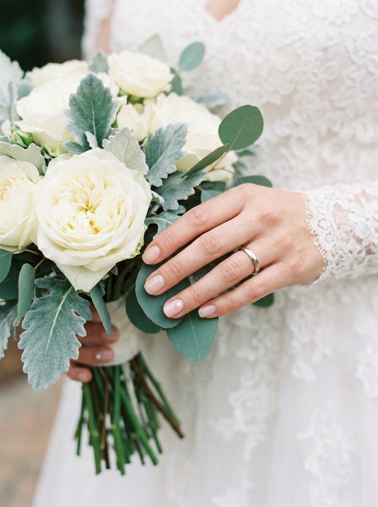 Bride's hand with a subtle pearl accent nail near her bouquet