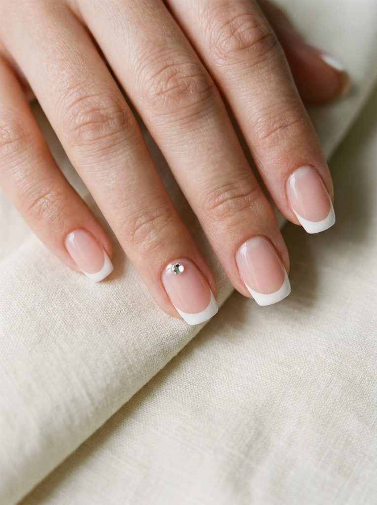 Close-up of a classic French manicure with a single rhinestone accent
