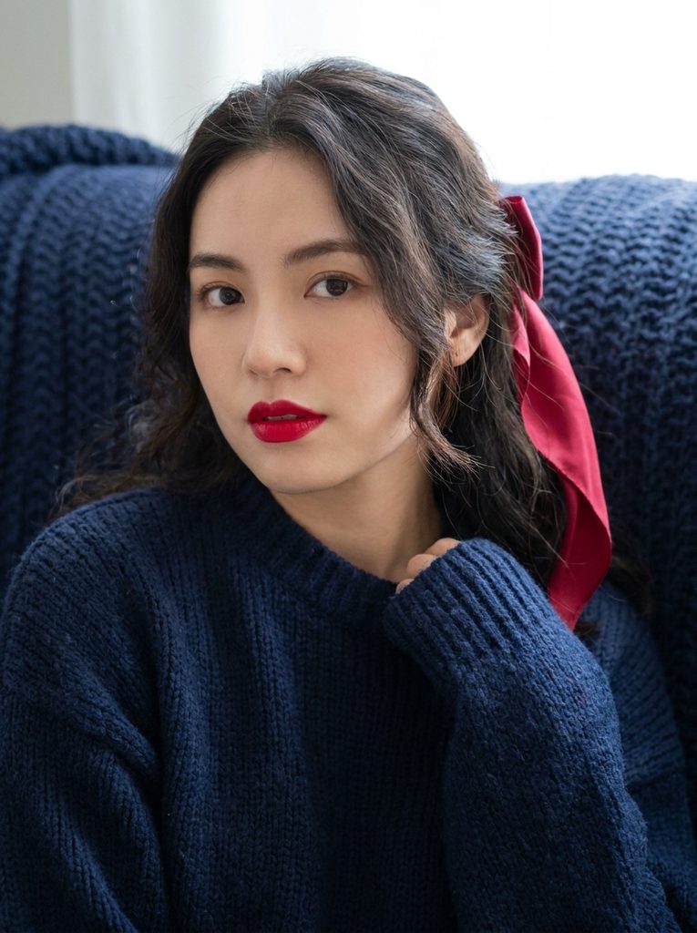Portrait with cherry red lips and a red silk hair ribbon against a navy knit