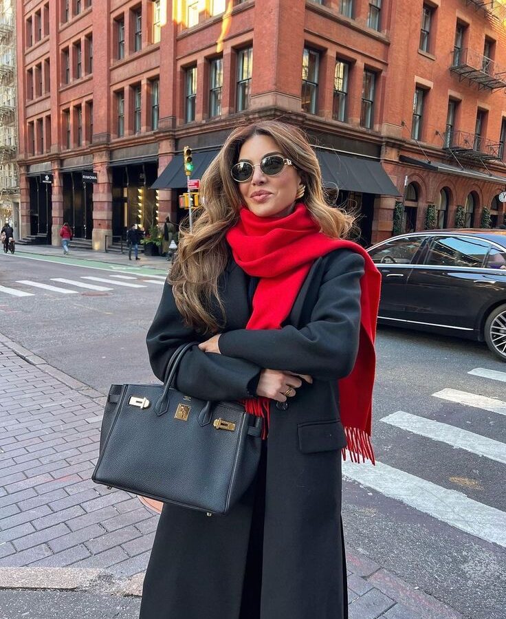 Woman in a midnight blue wool coat with a cherry red handbag and scarf on an autumn street