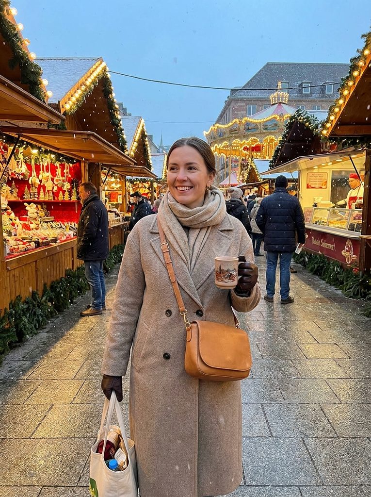 Woman wearing a tan mid-size crossbody bag while holding a mug and a canvas tote at a Christmas market