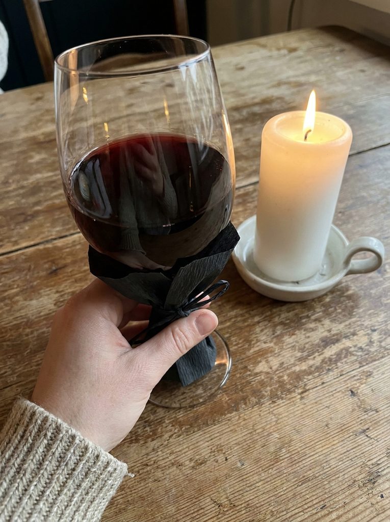 Hand holding a glass of red wine with a dark matte crepe sleeve beside a candle