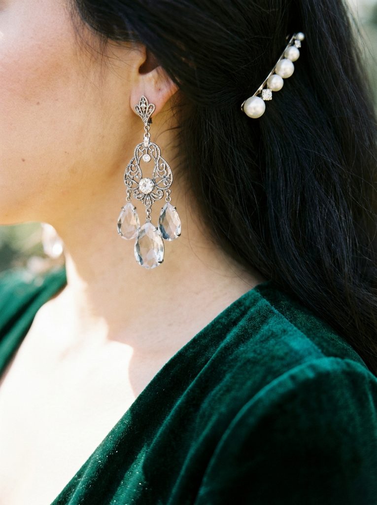 Close-up of crystal drop earrings and a pearl hair pin with a dark velvet neckline