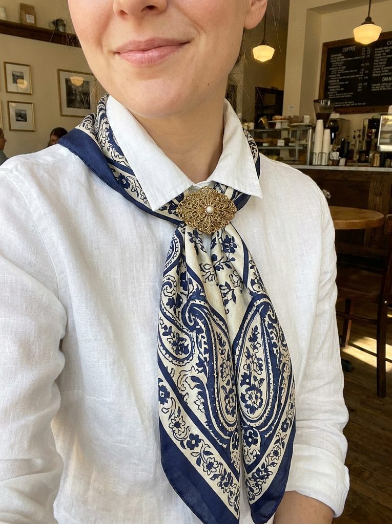 Navy and cream silk scarf fastened with a gold brooch on a white shirt wearing woman